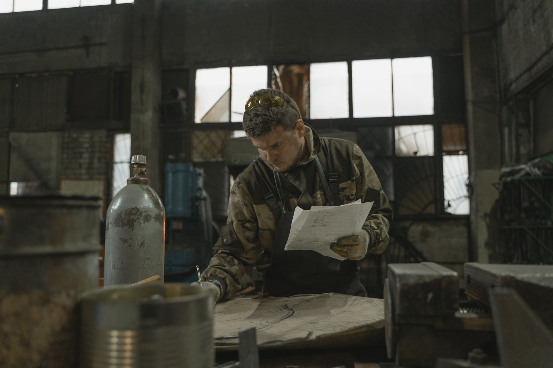 A blacksmith focused on drawing and metalwork inside a rustic workshop.