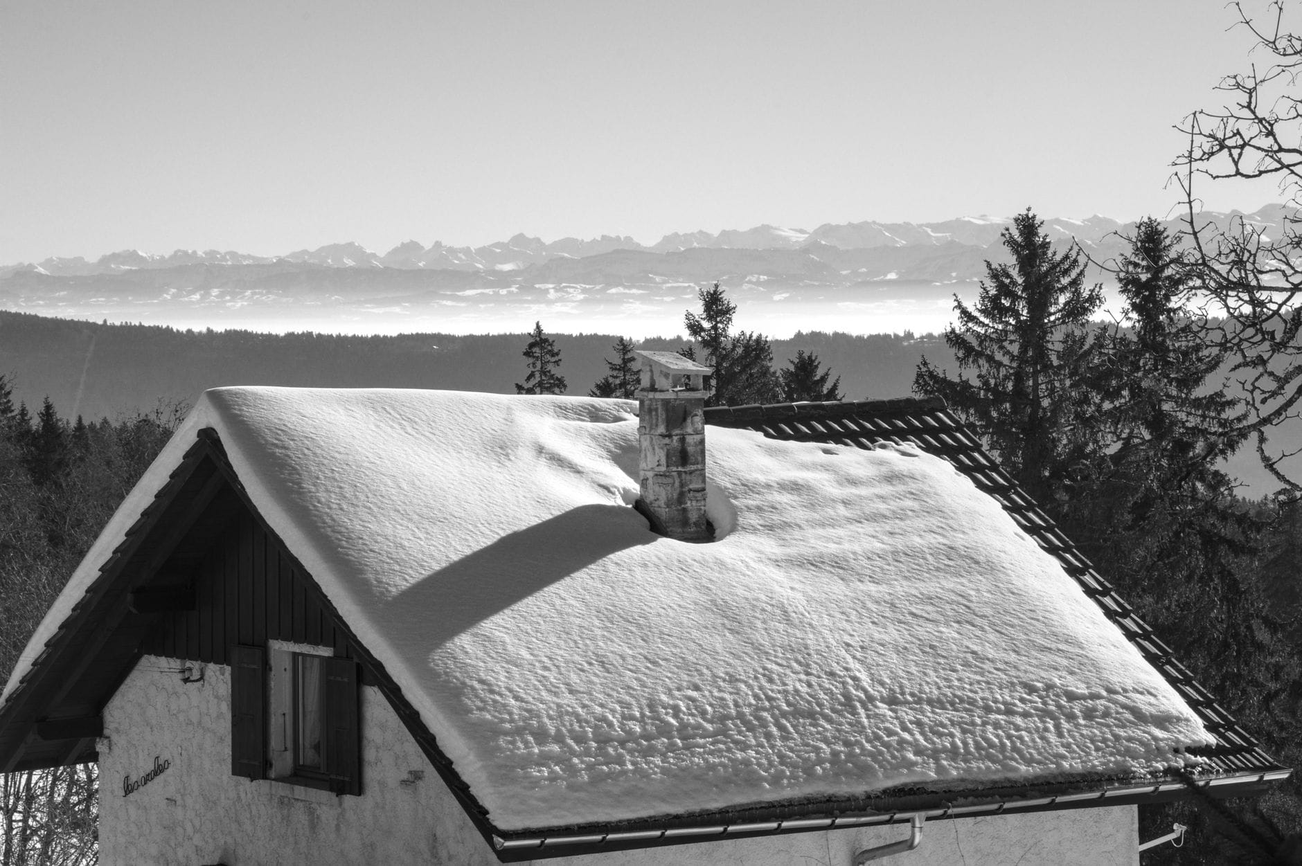 A serene black and white image of a snow-covered cabin roof with distant mountain views.